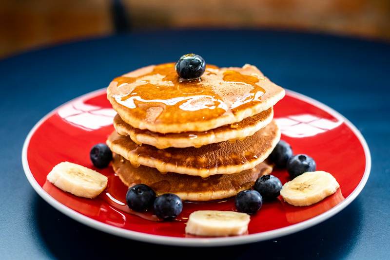 A stack of pancakes with blueberries and banana slices on a red plate