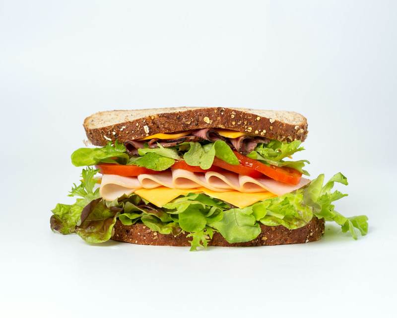 A tall sandwich with ham, cheese, tomato and lettuce on a white background